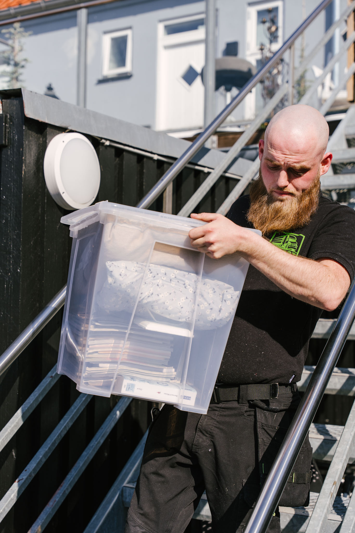 Flyttemand bærer en plastkasse ned ad en udvendig trappe